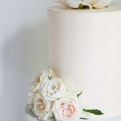 Valkoinen pitkä hääkakku pionilla ja pienillä ruusuilla