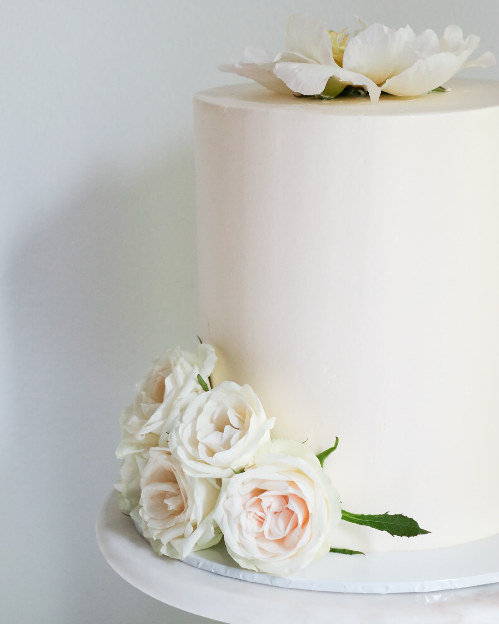 Valkoinen pitkä hääkakku pionilla ja pienillä ruusuilla