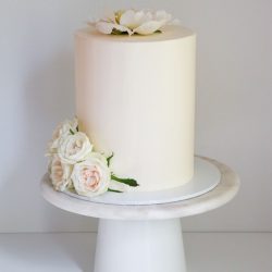 Valkoinen pitkä hääkakku pionilla ja ruusuilla