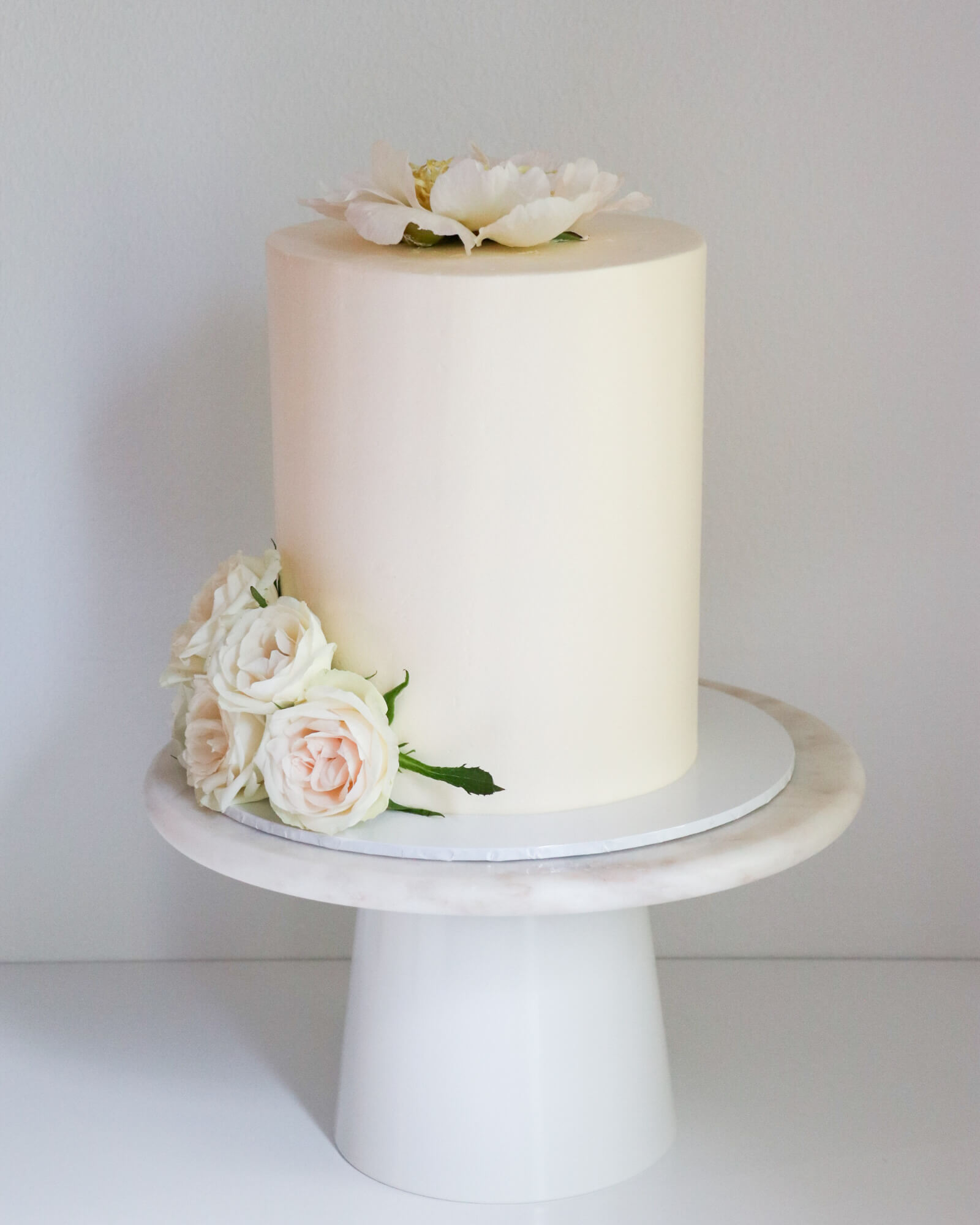 Valkoinen pitkä hääkakku pionilla ja ruusuilla