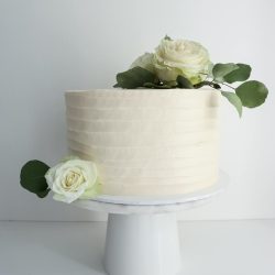 Valkoinen pyörre hääkakku ruusuilla ja eukalyptuksen oksilla