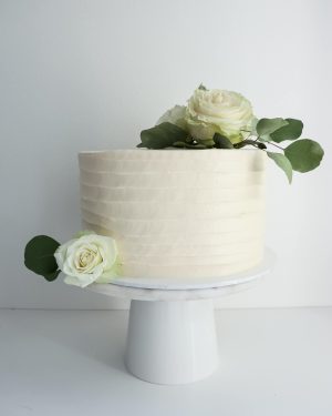 Valkoinen pyörre hääkakku ruusuilla ja eukalyptuksen oksilla